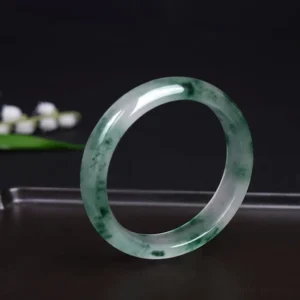Handcrafted jade bangle showing delicate floating flower design and glossy polished surface