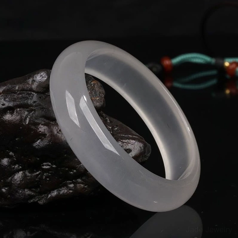 Single jade bangle in side oblique view highlighting smooth rounded rim and milky white translucent texture