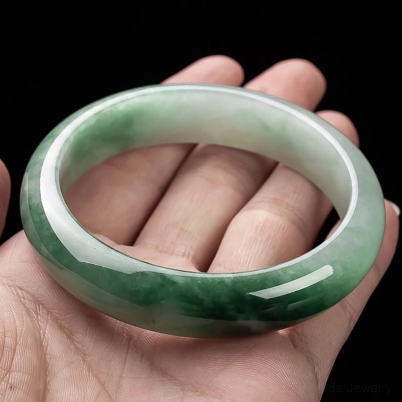 Jade bangle bracelet on human palm showing size reference and natural green color with bold dark patches