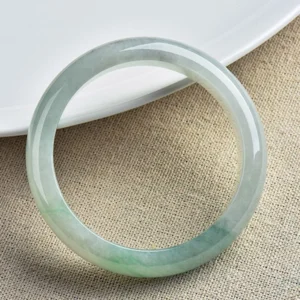 Translucent jade bangle bracelet with floating green patterns, photographed from three-quarter angle on white porcelain plate