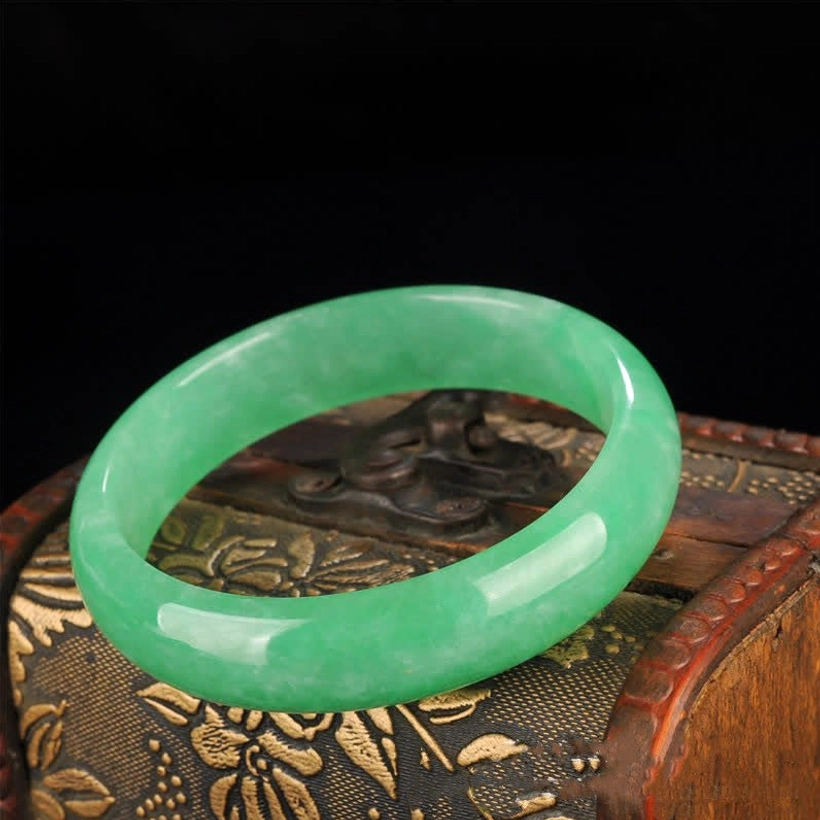 Light green jade bangle bracelet with dark green vein patterns, displayed on natural wood jewelry box background
