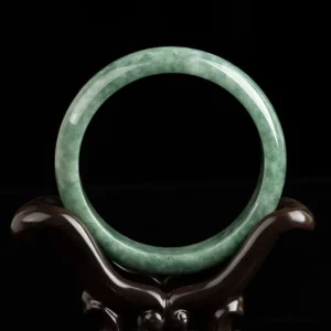 Green jade bangle bracelet front view on wooden display stand, showcasing smooth polished finish and authentic jade patterns