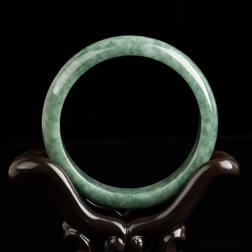 Green jade bangle bracelet front view on wooden display stand, showcasing smooth polished finish and authentic jade patterns