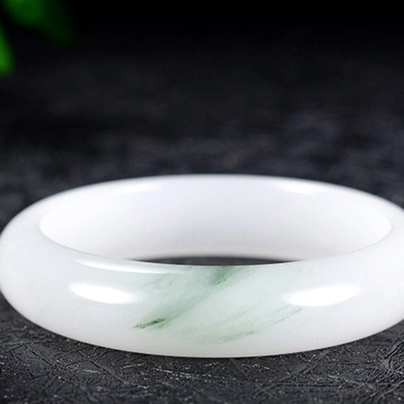 Highly polished jade bangle featuring smooth white base with thin green veins in flat overhead perspective