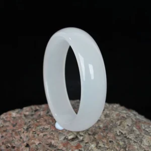 Natural white jade bangle bracelet front view, polished smooth finish against rough stone texture and dark background