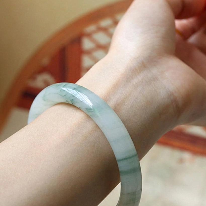 Natural jade bangle worn on right wrist with classic round band design against traditional Chinese arch window background