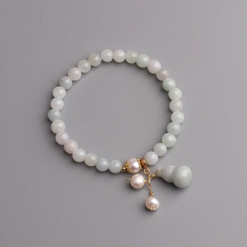 Jade bead bracelet with pearl and gourd pendant flat lay on neutral gray background showing matte off-white jade beads and gold hardware