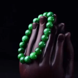 Green jade beaded bracelet side view displayed on wooden hand sculpture showing glossy spherical jade beads in studio setting