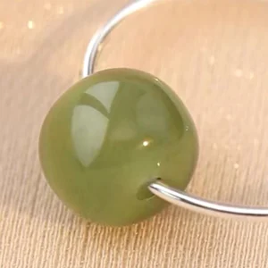 Close-up macro view of jade bead sterling silver earring detail - glossy round green jade stone on polished silver hoop with linen background