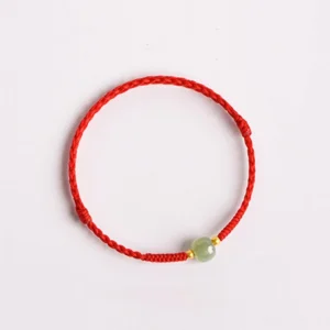Top-down flat lay of jade barrel bead lucky bracelet with red woven cord on minimalist background