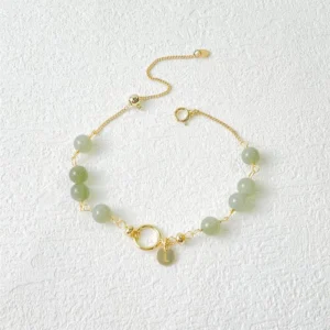 Light green jade beads with gold-filled hardware and adjustable chain on textured off-white surface