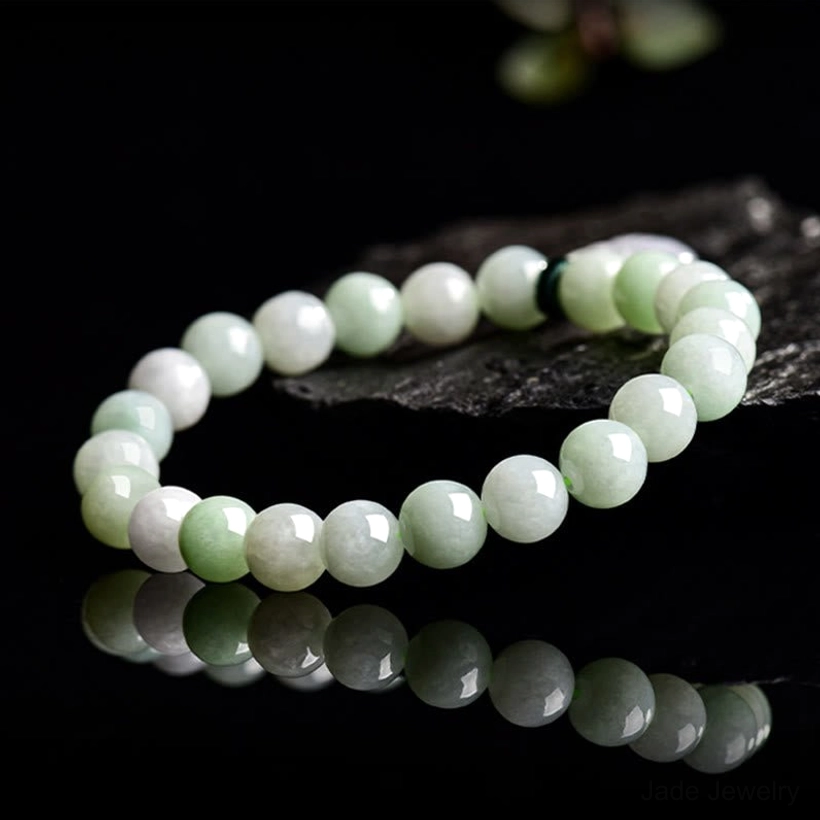 Gradient green-white polished jade beaded bracelet displayed on dark wooden surface with reflection, showing bead uniformity and quality