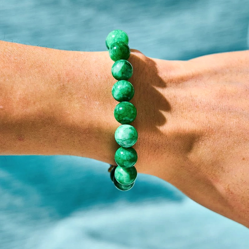 Plain green jade beaded bracelet on human wrist with water backdrop showing natural stone detail