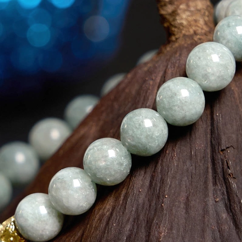 Detailed close-up of polished light green jade beads with gold metal end cap on dark wood background