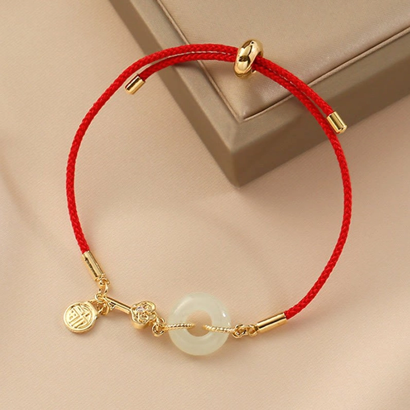 Close-up detail of 18K gold-plated hardware and jade peace buckle on red cord bracelet