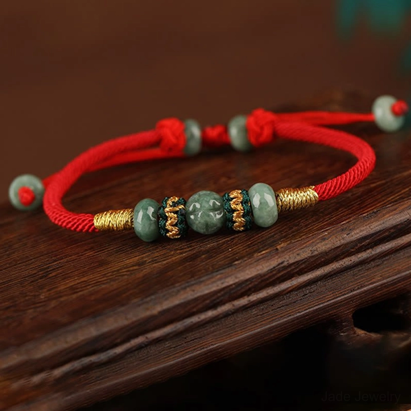 Adjustable jade prosperity bracelet with gold braided accents and dangling jade bead end, flat lay wooden background