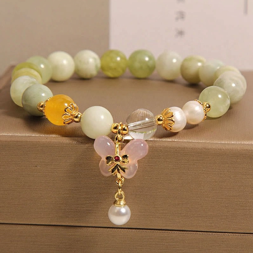 Close-up detail of jade bracelet butterfly charm with pearl drop and clear crystal spacer bead, gold-tone hardware