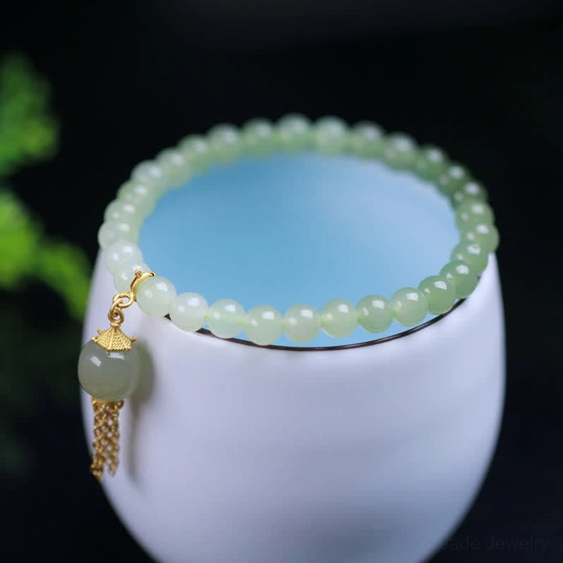 Hetian jade bracelet overhead top view circled around white ceramic cup rim, jade beads with sterling silver gold tassel charm