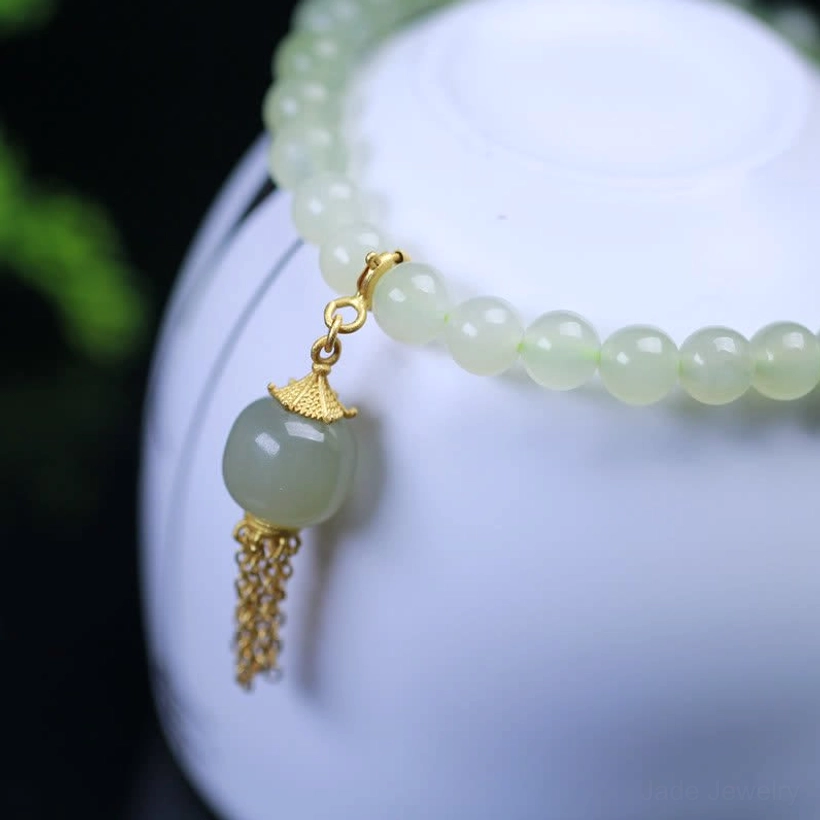 Close-up macro view of Hetian jade bracelet charm, large central jade bead with ornate sterling silver cap and dangling tassel detail