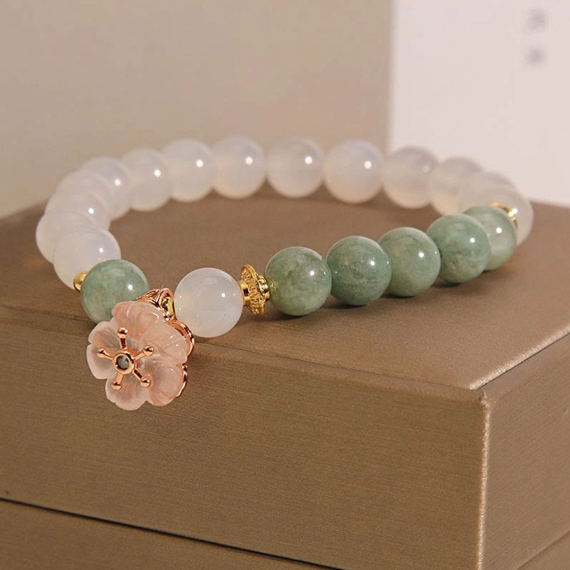 Three-quarter angle of white agate jade bracelet featuring delicate pink flower charm and rose gold spacer beads