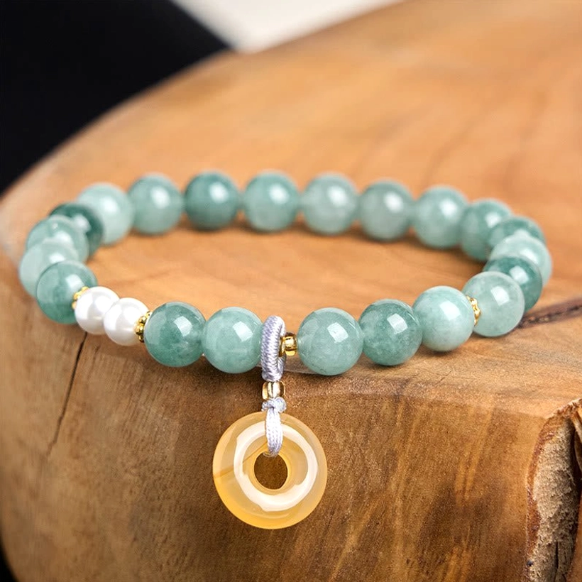 Close-up overhead view of teal jade beads with white pearl accents and yellow peace buckle pendant on polished wooden surface