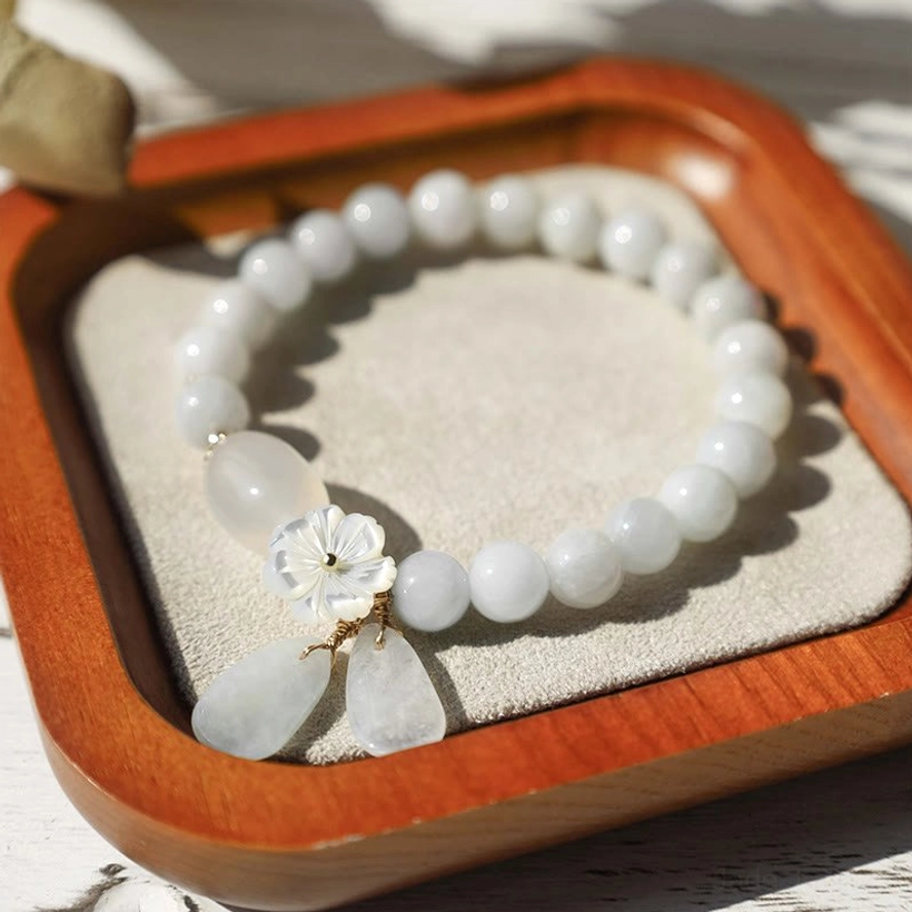Pale blue jade beaded bracelet with shell flower ornament and teardrop pendants on velvet-lined wooden tray