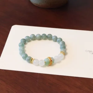 Mixed green and white jade beaded bracelet with gold decorative accents displayed on dark wood table with white card