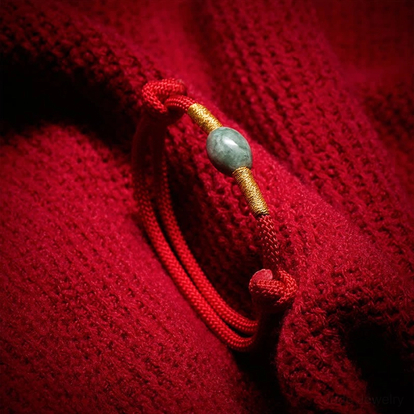 Close-up detail of red jade protection bracelet showing braided knots and gold-tone metal accents on red fabric