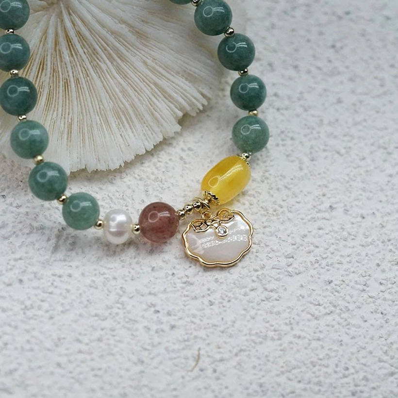 Full jade Ruyi lock bracelet with sea shell backdrop on sand - flat lay top-down view