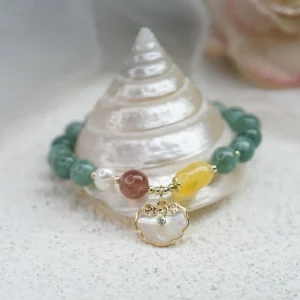 Jade luck bracelet with mixed gem accents and shell Ruyi pendant charm on conch shell and sand surface - low angle view