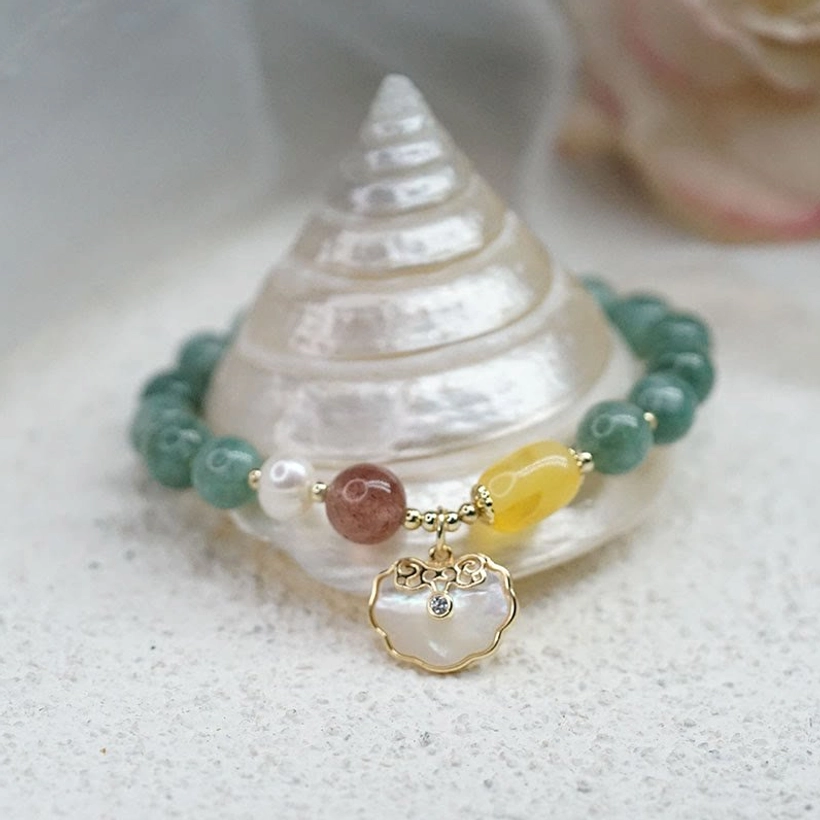 Jade luck bracelet with mixed gem accents and shell Ruyi pendant charm on conch shell and sand surface - low angle view