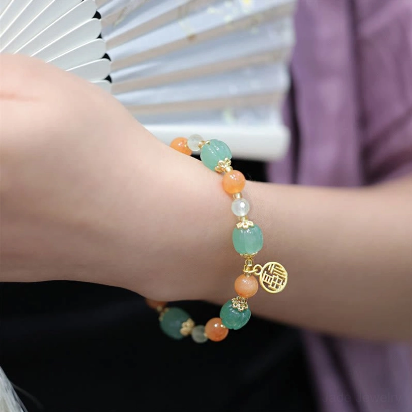 Fu character jade bracelet worn with Chinese fan background, showing gold charm on outer wrist with coordinated green and orange tones