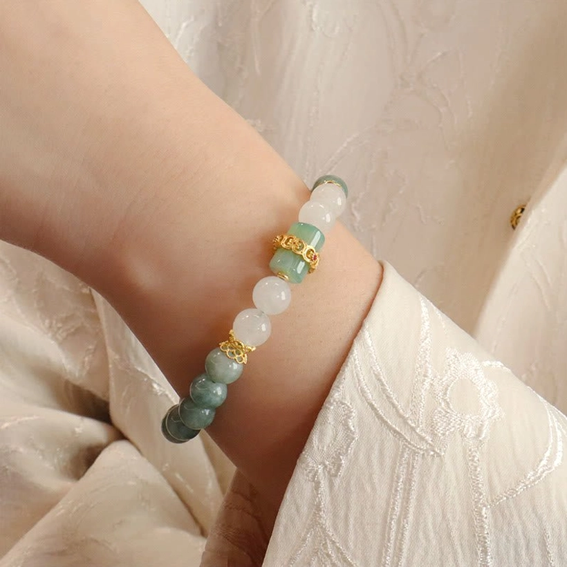 Jade peace buckle bracelet worn on wrist with green and white jade beads and gold metal details on beige traditional fabric