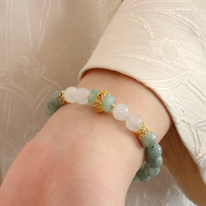 Jade beaded bracelet side close-up showing mixed green and white jade beads with gold metal decorations on embroidered beige fabric