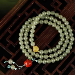 Handmade jade Laughing Buddha bracelet with smooth light green beads, amber decorative center bead, red Buddha charm, turquoise tassel on carved wooden lattice background