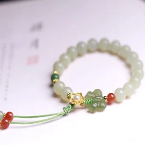 Handmade jade butterfly beaded bracelet with metal flower accent and green tassel detail on calligraphy paper