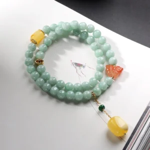 Top-down view of natural jade beads with red agate butterfly charm and amber accent on white paper background