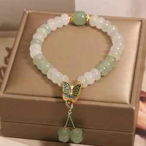 Flat lay view of two-tone jade beaded butterfly bracelet inside luxury brown jewelry box with gold charm