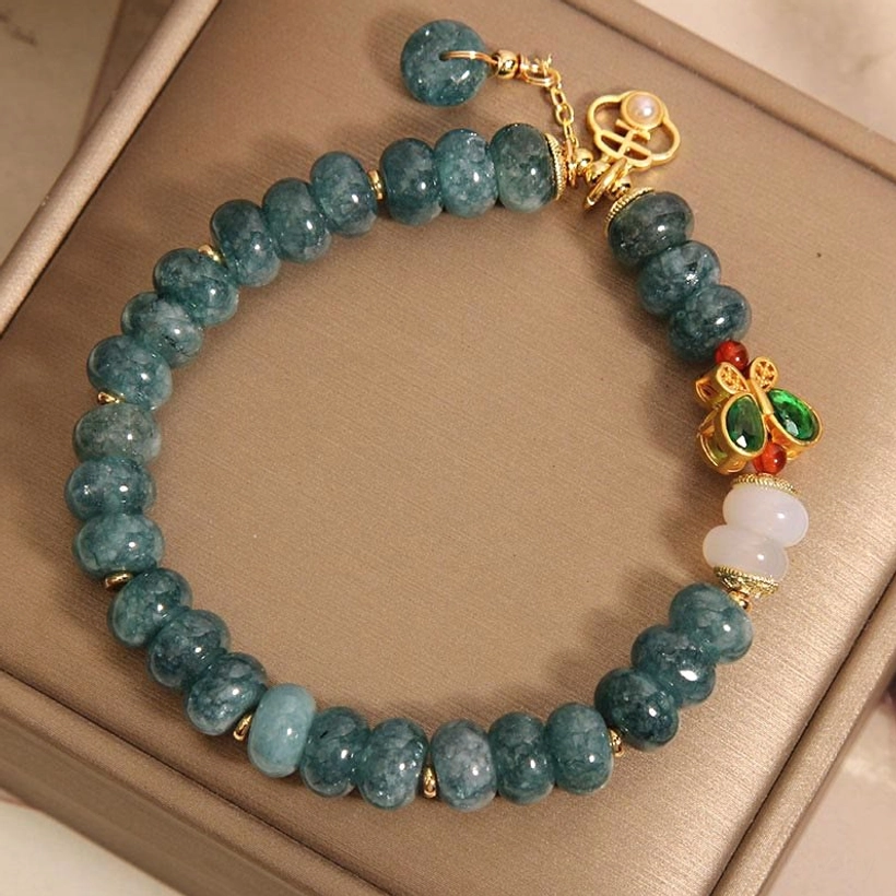 White jade and agate bracelet reverse side showing butterfly charm detail, displayed in brown jewelry box angled view