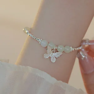 Close-up side view of jade butterfly bracelet on wrist with dangling silver butterfly charm and feminine setting