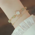 Double-layer jade butterfly luck bracelet with 14K gold chain and crystal butterfly charm, worn on wrist with ruffled satin sleeve