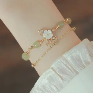 Double-layer jade butterfly luck bracelet with 14K gold chain and crystal butterfly charm, worn on wrist with ruffled satin sleeve