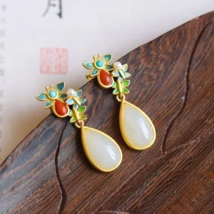 Close-up oblique view of jade butterfly drop earrings on dark wood, featuring enamel butterfly stud with red agate stones and white jade teardrop pendant