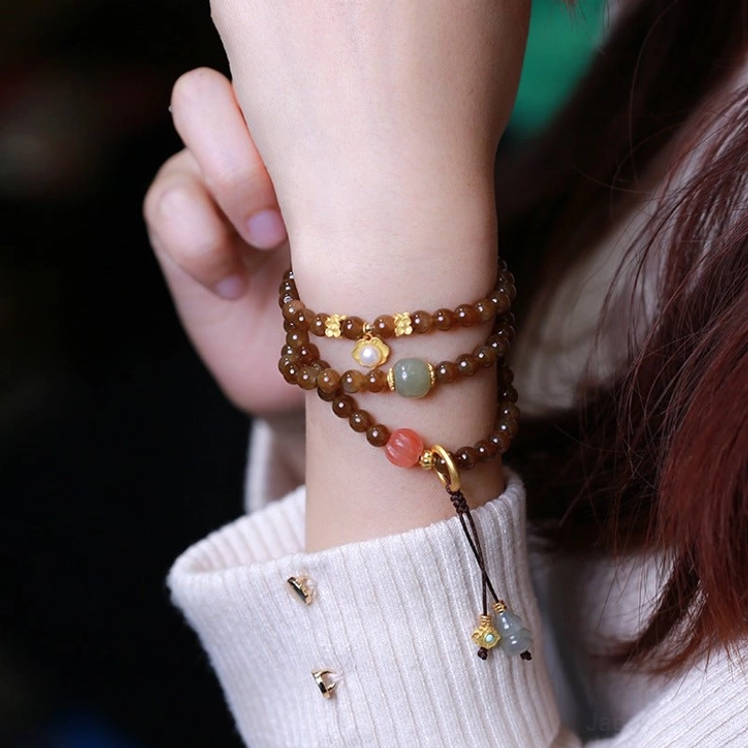 Double-wrap jade butterfly gourd bracelet with gold hardware and decorative tassel pendant worn on wrist side view