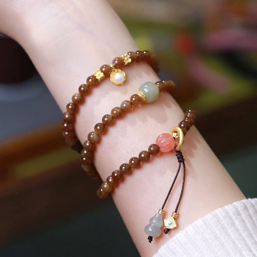 Multi-strand jade butterfly gourd bracelet wrapped around wrist with gold spacer beads and pearl accents overhead view