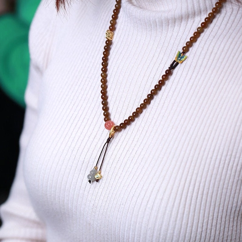Jade butterfly gourd prosperity necklace worn as statement piece on upper body with white knitted top showing front styling