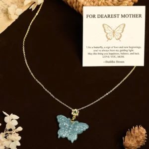 Jade butterfly mom necklace with gold-tone chain displayed on dark brown backdrop with dried botanical elements, flat lay composition