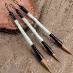 Set of jade calligraphy brush pens with hanging lanyards displayed on carved wooden backdrop, natural stone writing brushes