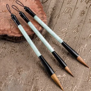 Set of jade calligraphy brush pens with hanging lanyards displayed on carved wooden backdrop, natural stone writing brushes