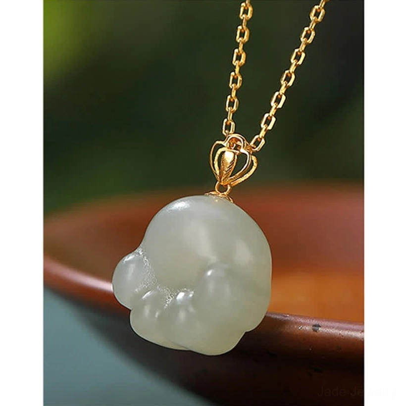 Hetian white jade cat paw pendant three-quarter view on brown ceramic plate showing carved paw pad details and gold metal bail